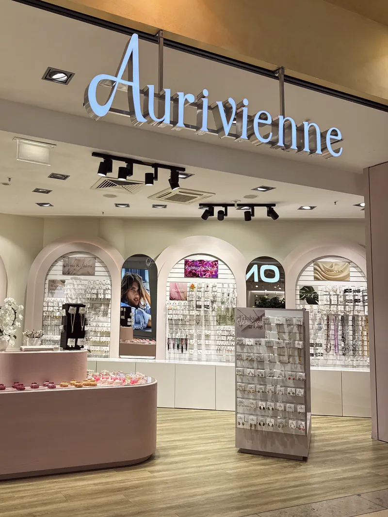 Der Eingang von Aurivienne in der Thier-Galerie: beleuchteter Schriftzug über rosa Rundbögen, davor ein rosa Verkaufstisch mit Schmuck.